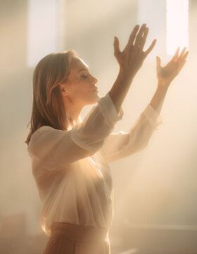 Young Woman Worshipping God with Raised Hands in Warm Light, Christian Faith and Praise Concept