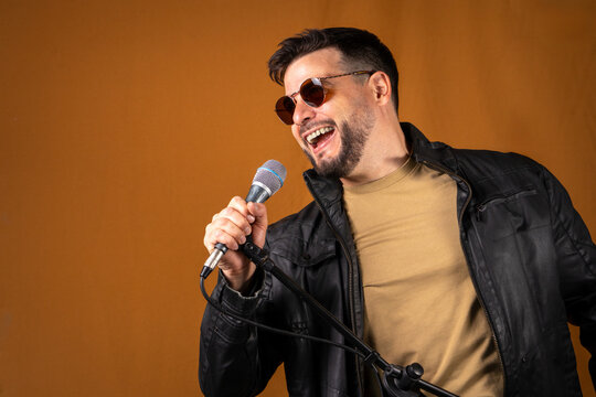 Hombre rockero con chaqueta de cuero y lentes cantando en&eacute;rgicamente con su microfono