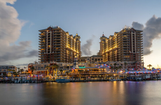 The scene captures a waterfront view with lit-up buildings reflecting in the calm waters during twilight. The sky has a gradient of soft blues and purples, creating a serene backdrop 