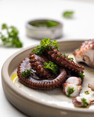 Boiled octopus tentacles and sliced pieces on ceramic plate close up. Olive oil and parsley dressing