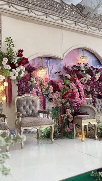 Elegant floral wedding stage featuring plush vintage chairs and lush blooming rose arrangements creates a romantic atmosphere for this high definition motion video captured at a beautiful reception.
