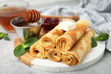 Tasty rolled crepes with honey, jam, butter and mint leaves served on light grey table, closeup © New Africa