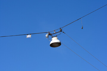 Obraz premium Vintage industrial street light fixture suspended by electrical cables against a clear blue sky background in an urban area