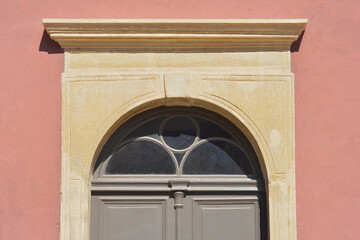 Detail of a traditional arched stone portal and lintel above a grey wooden door set into a salmon...