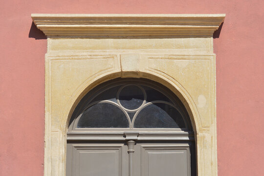 Detail of a traditional arched stone portal and lintel above a grey wooden door set into a salmon pink building facade