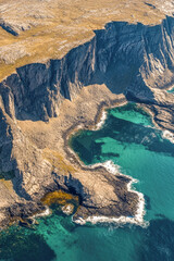 Naklejka na ściany i meble Aerial view of a rocky coastline with blue water, suitable for use in travel or landscape photography. vertical frame