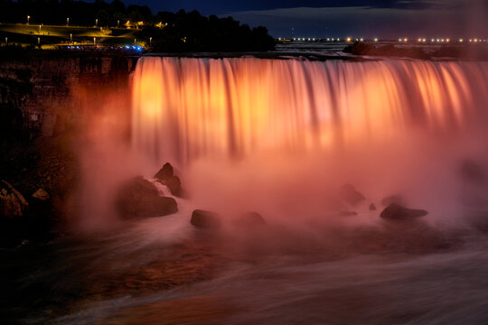 Niagara Falls illuminated orange at night.