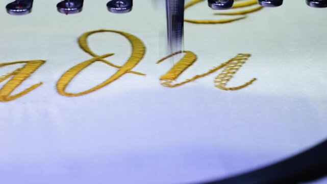 Machine embroidery of text with gold thread on a white satin robe. Preparation for the wedding day. Elegant bridal lingerie. Close-up.