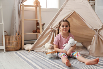 Little girl playing with toys near toy wigwam in playroom, space for text © New Africa