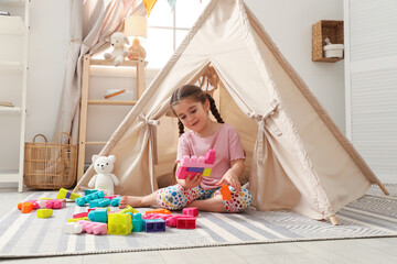 Little girl playing with building blocks near toy wigwam in playroom © New Africa