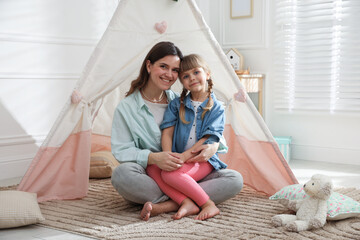 Mother and her daughter near toy wigwam at home © New Africa