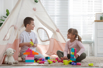 Little kids playing with building blocks near toy wigwam at home © New Africa