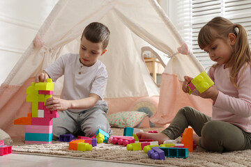Little kids playing with building blocks near toy wigwam at home © New Africa