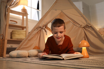 Little boy reading book near toy wigwam at home © New Africa