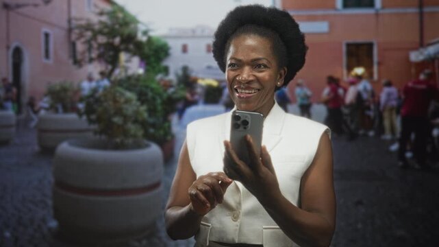 Woman holding smartphone and tapping screen with hands while smiling in a crowded street plaza; joyful connection.