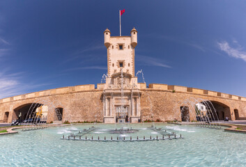 Panoramic view of Puerta de Tierra in Cadiz, Spain, with the historic fortress gate and fountain under clear blue sky.