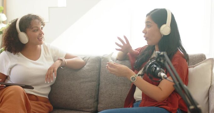 Talking right woman gesturing and miming call, left woman listening with headsets on sofa, boom mic