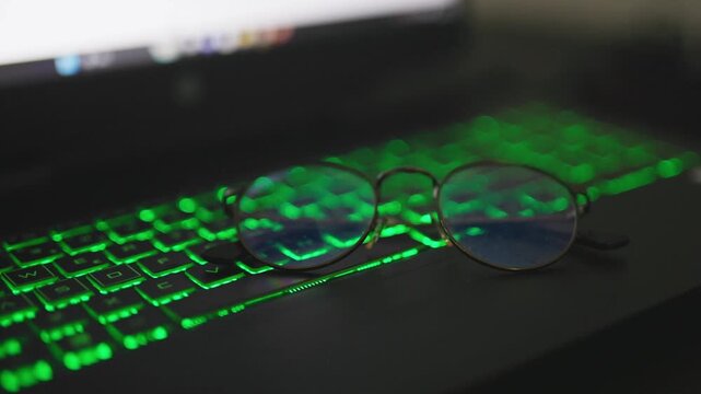 Close up of green backlit gaming keyboard and eyeglasses