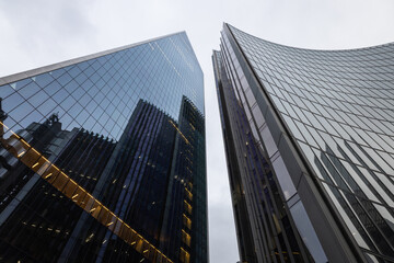 Fototapeta premium Looking up at towering glass office buildings against a cloudy sky
