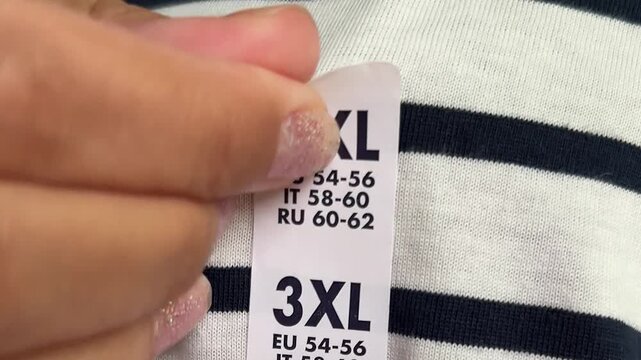 4K video close up. Fat man in white T-shirt with stripes removes 3XL sticker. Concept of Black Friday sale, buying new clothes of Extra Large size 3 XL, shopping in mall, fitting, weight loss. Shop