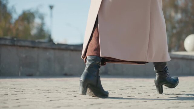 Dynamic shot of stylish outfit and stride. Chic footwear and clothing in bright urban setting. Confident person walking through sunlit city square wearing fashionable attire and footwear