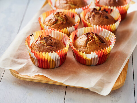 Freshly baked muffins are arranged in vibrant liners on a wooden tray. Ideal for restaurant menus, food blogs, and social media sharing