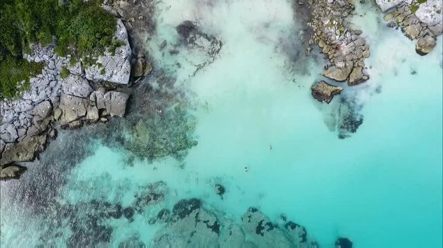 An aerial view reveals a stunning coastline where turquoise waters meet rocky shores and lush greenery, creating a serene and idyllic tropical paradise.