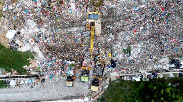 Large scale landfill operation with excavator and garbage trucks working at waste disposal site