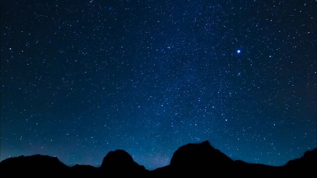 A vast, star-filled sky dominates the scene, with a dark silhouette of mountains along the bottom edge, creating a sense of awe and wonder.