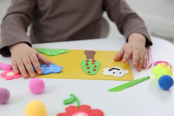 Fototapeta premium Little girl making picture with colorful play dough at white table, closeup