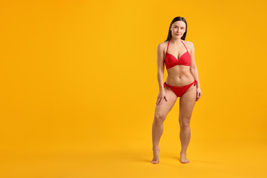Beautiful woman in stylish swimsuit posing on yellow background. Space for text