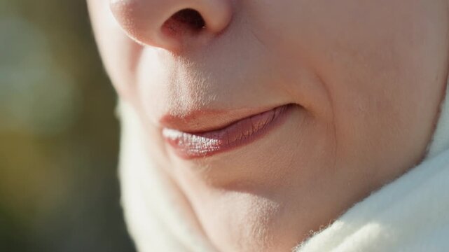 Closeup white woman showing glossy lips outdoors with soft daylight, lips settled in satin finish, subtle contour visible, scarf framing jawline, model pausing to inspect result, quiet satisfied