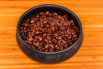 Fototapeta premium Roasted coffee beans in black clay bowl on wooden surface