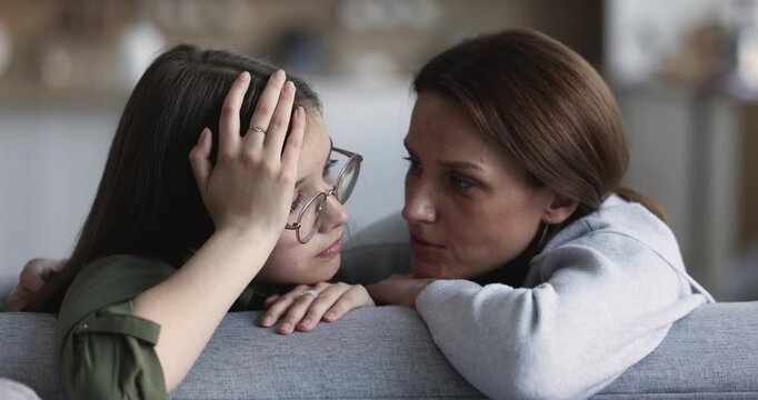 Closeup mother gently stroking hair of sad teen daughter during talk, comforting through touch and calm conversation, providing emotional support, giving advice, showing parental care and love at home