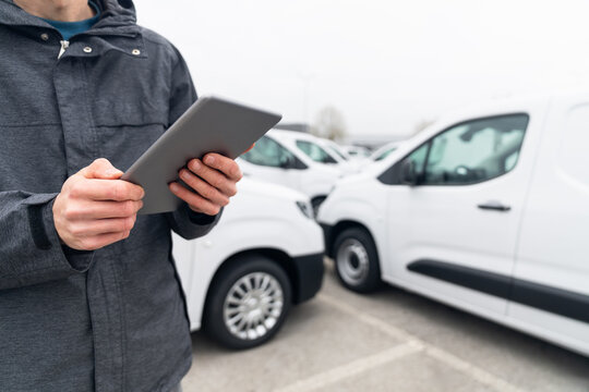 Fleet manager with digital tablet supervising rows of white delivery vans