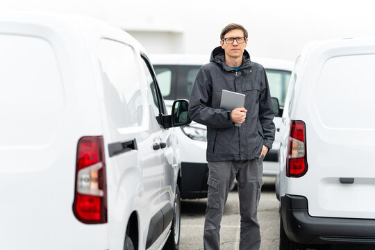 Fleet manager with digital tablet supervising rows of white delivery vans