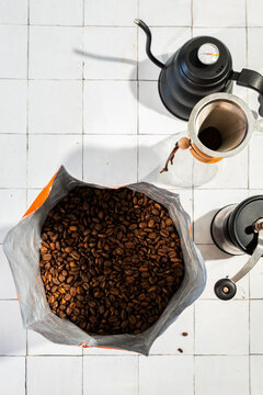 Coffee bean in a bag with a pour over coffee pot, grinder and kettle on a white tile surface 