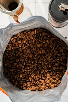 Coffee bean in a bag with a pour over coffee pot, grinder and kettle on a white tile surface 