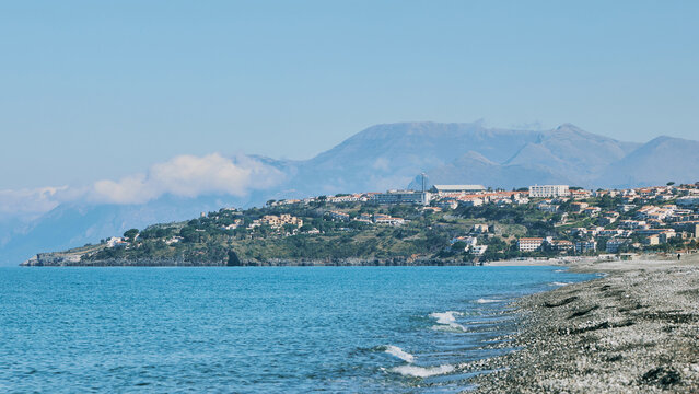Scenic view of Scalea town on a rocky cliff by the Tyrrhenian Sea in Calabria, Italy. Beautiful summer landscape with pebble beach and mountains.