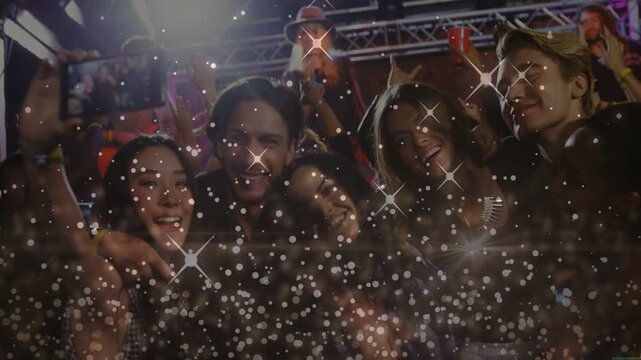 Vertical video: Group tweaking phone, posing selfie to catch performer at gig, sparkles over faces