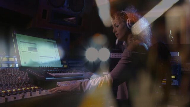 Female audio engineer adjusting console faders in studio, pressing play, monitoring playback