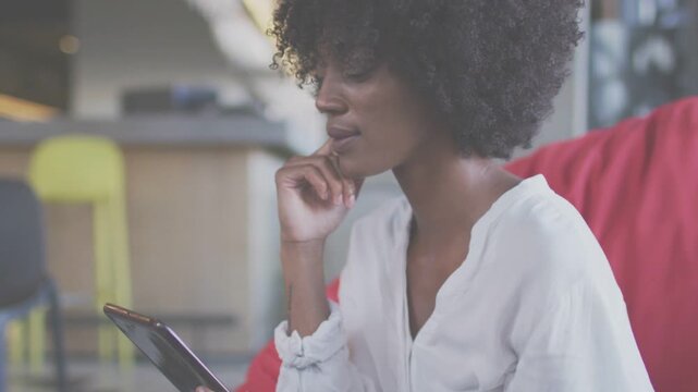 Adult woman resting chin, reading tablet on red seat in tech lounge, tapping screen, causing scroll