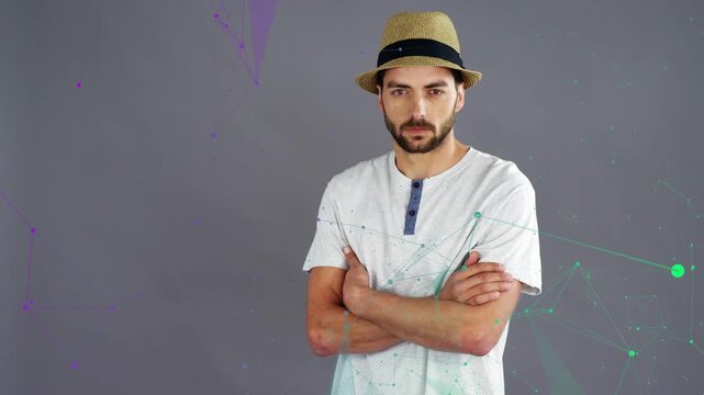 Male model taking camera cue, uncrossing arms, adjusting hat for fashion with teal nodes around him
