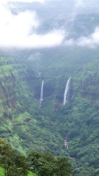 Varandha Ghat waterfall cascading down rugged cliffs in stunning vertical 4K. Misty monsoon clouds, lush green Sahyadri hills, and roaring water create a breathtaking wild nature scene.