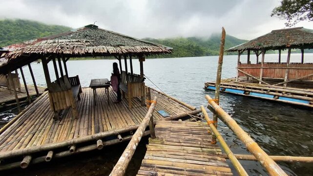 Traditional bamboo raft cottages floating on Lake Danao in the Philippines with misty mountain peaks hidden in clouds in the background