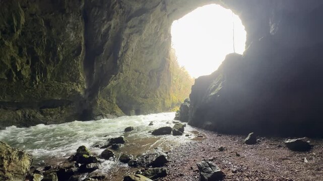 Stunning view from inside the large Weaver Cave, or Tkalca jama, in Slovenia. Bright sunlight illuminates the entrance as an underground river flows out