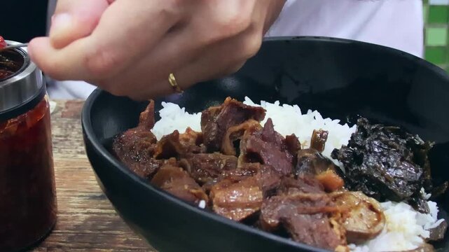 A hand adding chili paste to a bowl of braised beef (Ngau Lam) with Chu Hou paste, fermented spinach and rice. A traditional local Cantonese dish. Central, Hong Kong