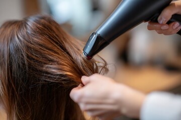 Naklejka premium Close-up of a hairdresser drying woman's brown hair with a black blow dryer. Professional beauty salon styling service