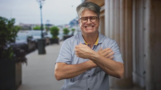 Man with glasses shrugs, hands raised and shoulders hunched in front of a building colonnade; playful.