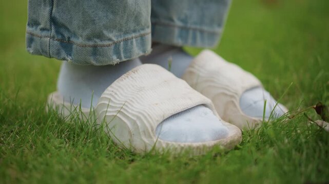 Feet in socks and slippers on grass, child wearing denim standing on lush lawn, closeup knit slipper detail with cotton socks, relaxed casual mood with soft sunlight and green texture